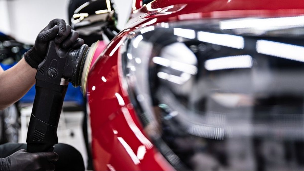Gloved hands using a machine polisher on glossy red car paint next to a headlight